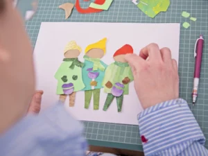 Eine Frau namens Frau Tulpe erstellt eine bunte Collage mit ausgeschnittenen Papierfiguren, die drei charakteristische Charaktere darstellen.
