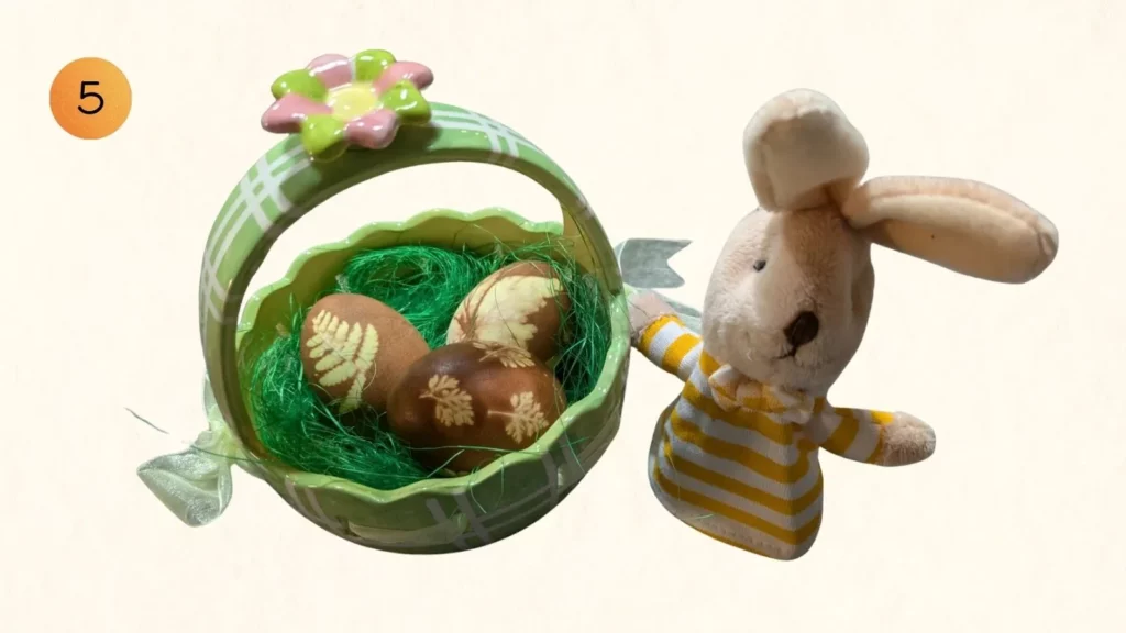 Fertig gefärbte Ostereier mit Blattmustern im grünen Körbchen neben einem Stoffhasen, Nummer 5.