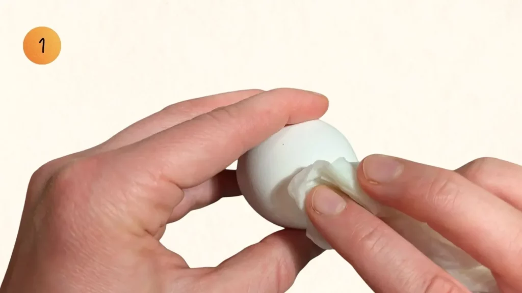 Anleitung zum Ostereier basteln für Kinder: Hände reinigen ein weißes Ei mit einem Tuch, mit Nummer 1.