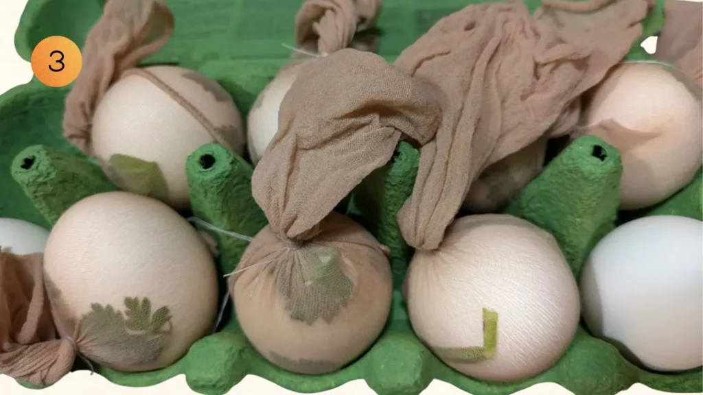 Weisse Eier in Nylonstrümpfen mit fixierten Blättern im Eierkarton für naturnahes Basteln in der Schweiz, Nummer 3.