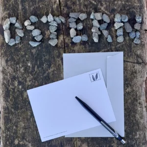 Postkarte mit Briefumschlag und Stift neben aus Steinen gelegtem Wort OSTERN auf Holz für Schweizer Schulbedarf.