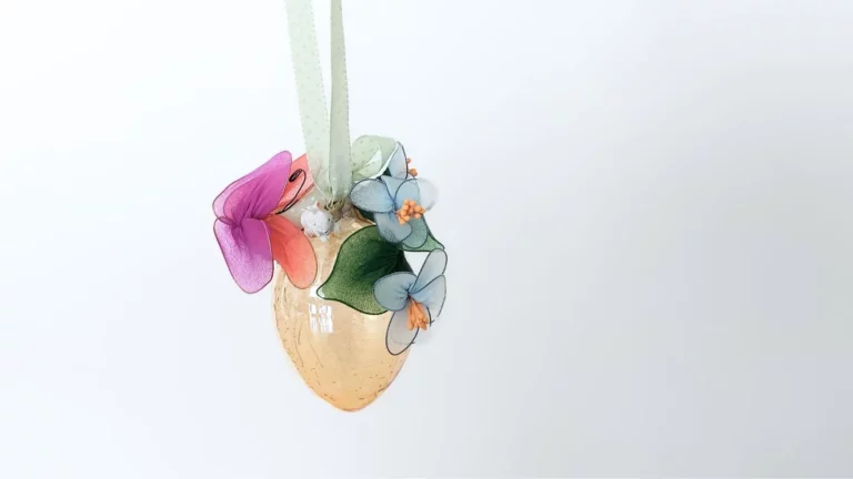 Ein hängendes, goldenes gelbes orangenes Osterei verziert mit bunten Textilblüten als Bastelidee für Schweizer Ostertraditionen.