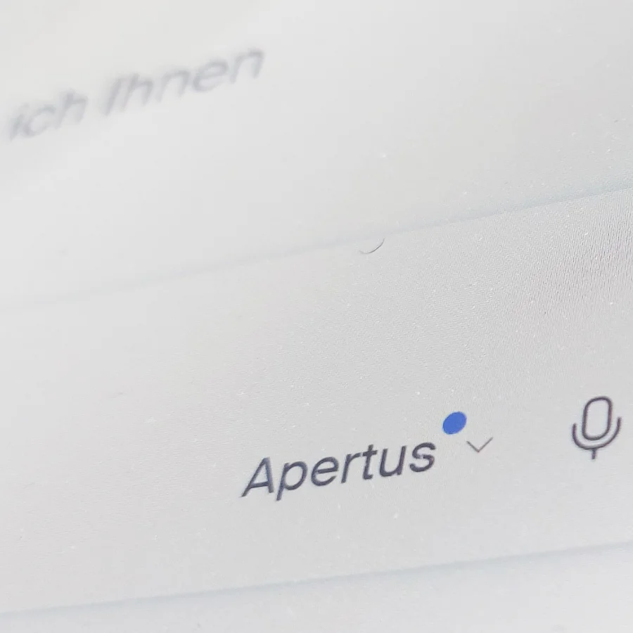 Eine detaillierte Nahaufnahme eines Suchfelds mit dem Namen "Apertus", einem blauen Dropdown-Pfeil und einem Mikrofon-Icon für die Sprachsteuerung.